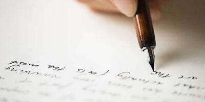A picture of someone with a fountain pen writing a letter.